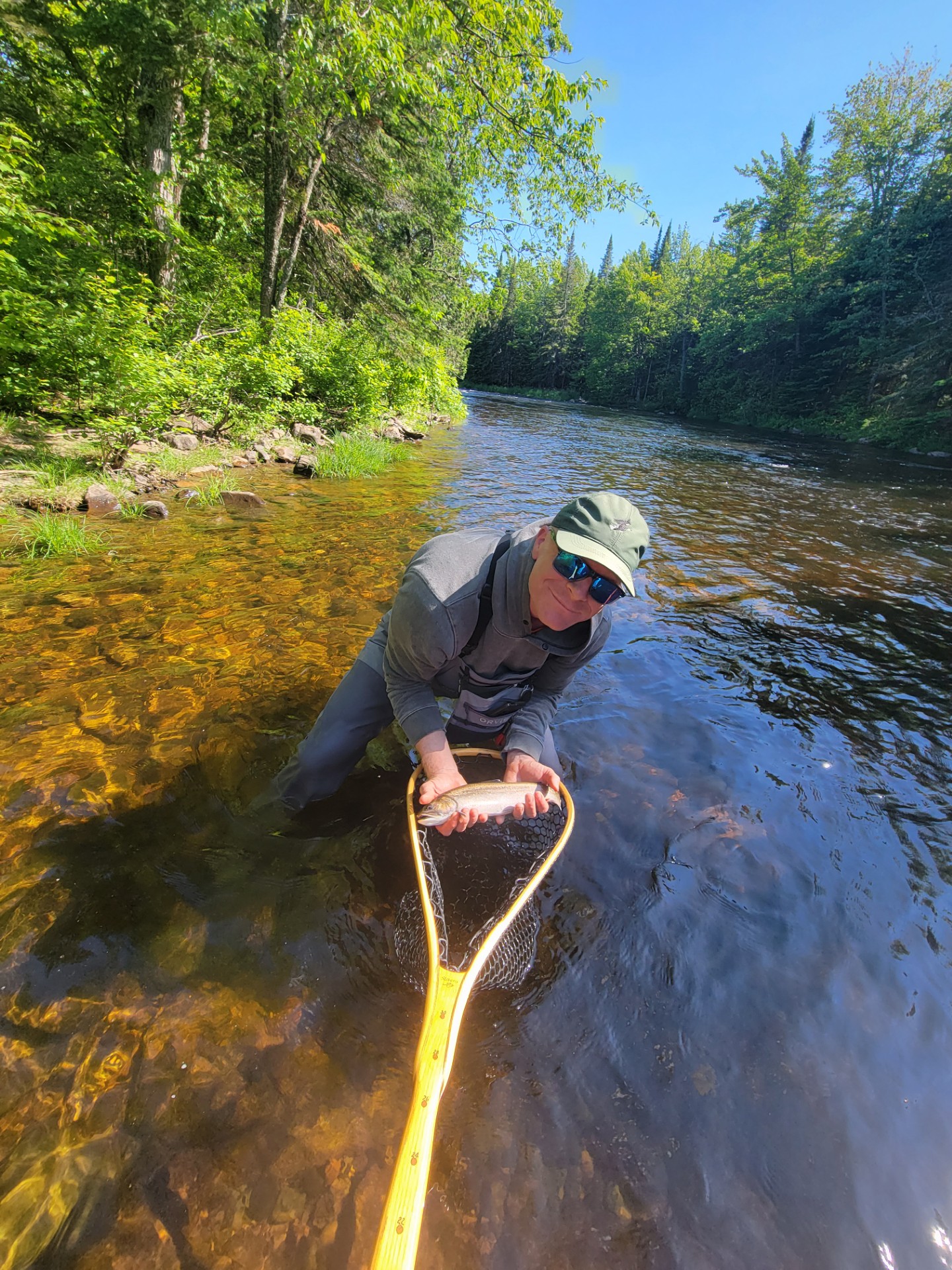 Smiling man holding fish above net in a river