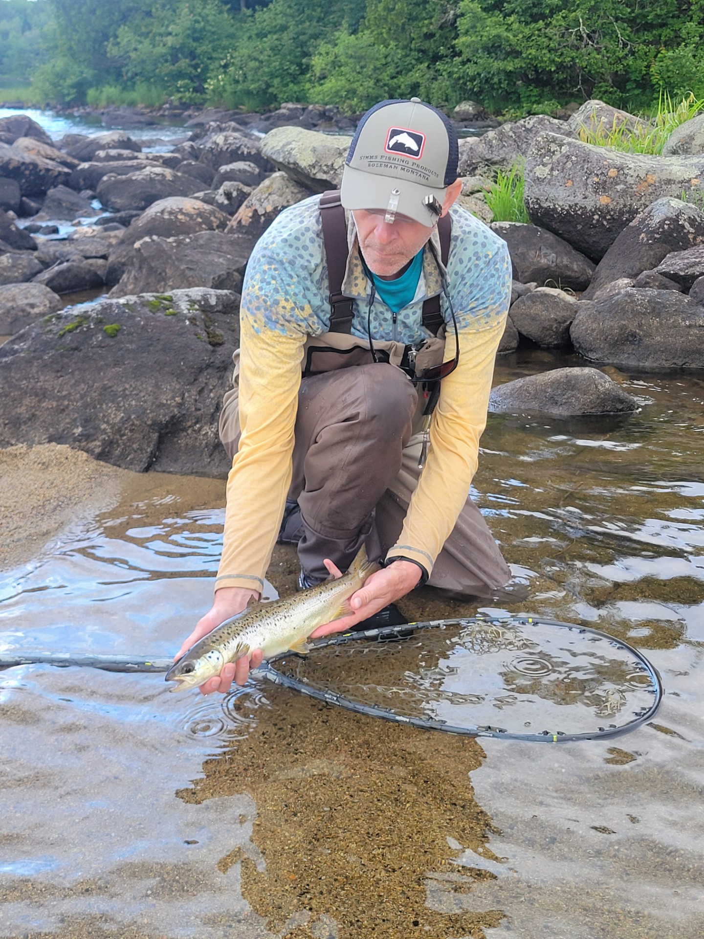 Fisherman kneeling in a river holding a fresh caught fish