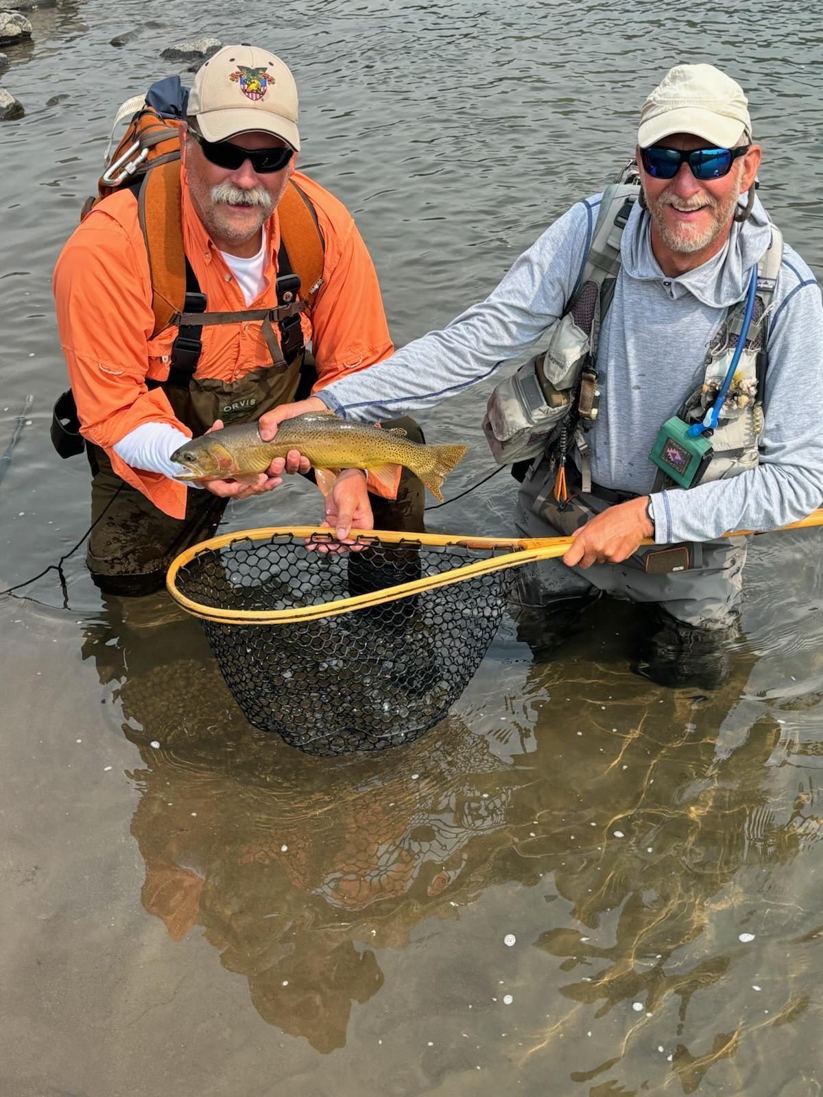 Two fisherman kneeling in a river holding a fresh caught fish