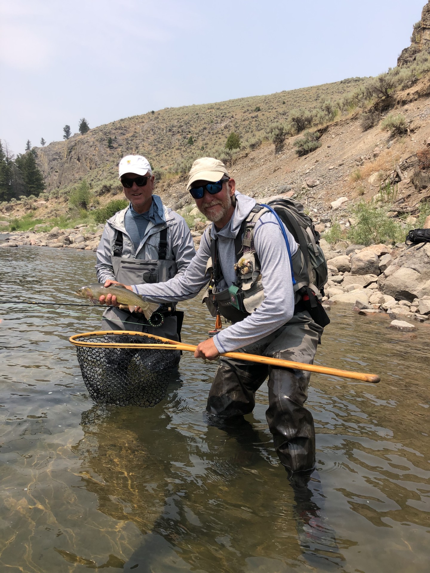 Two fisherman standingin a river holding a fresh caught fish